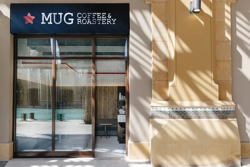 The Mug Coffee & Roastery storefront in daylight, black fascia sign on a sandstone building.